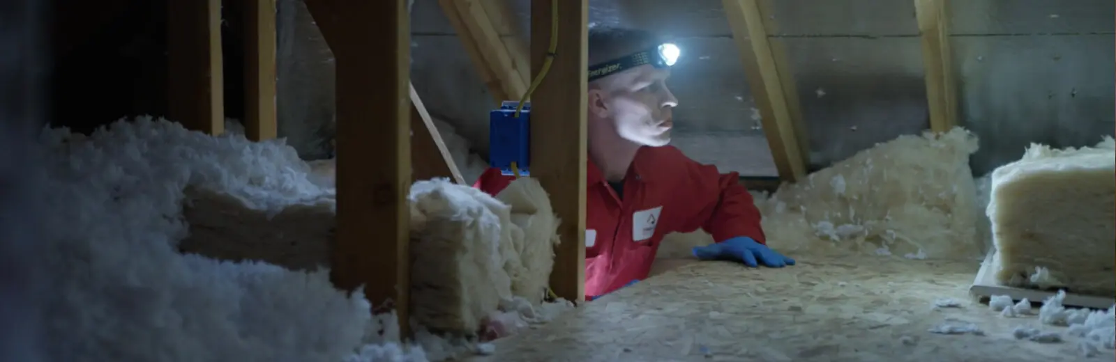 A man in a red jacket is standing in an attic.