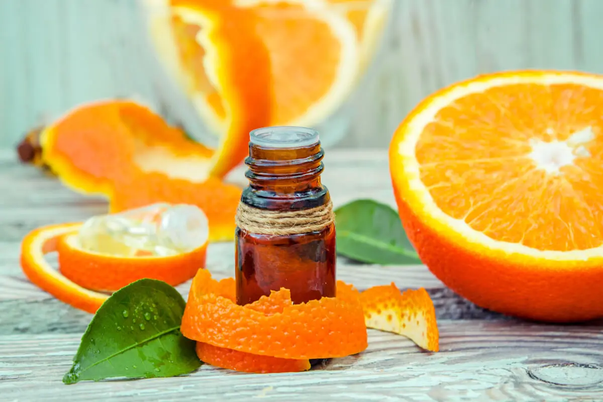 A bottle of essential oil and orange slices on a wooden table.