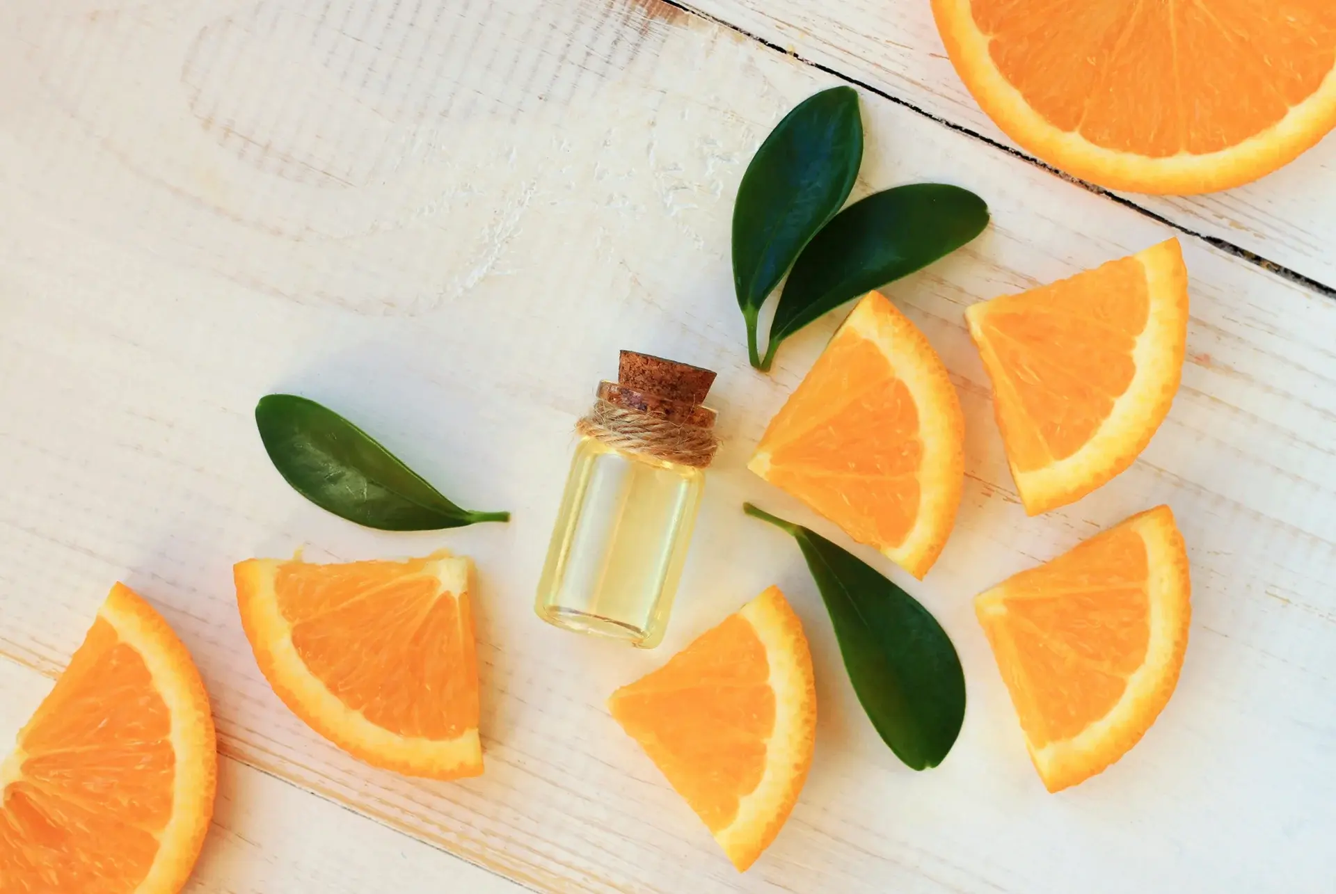 A bottle of essential oil and orange slices on a white background.